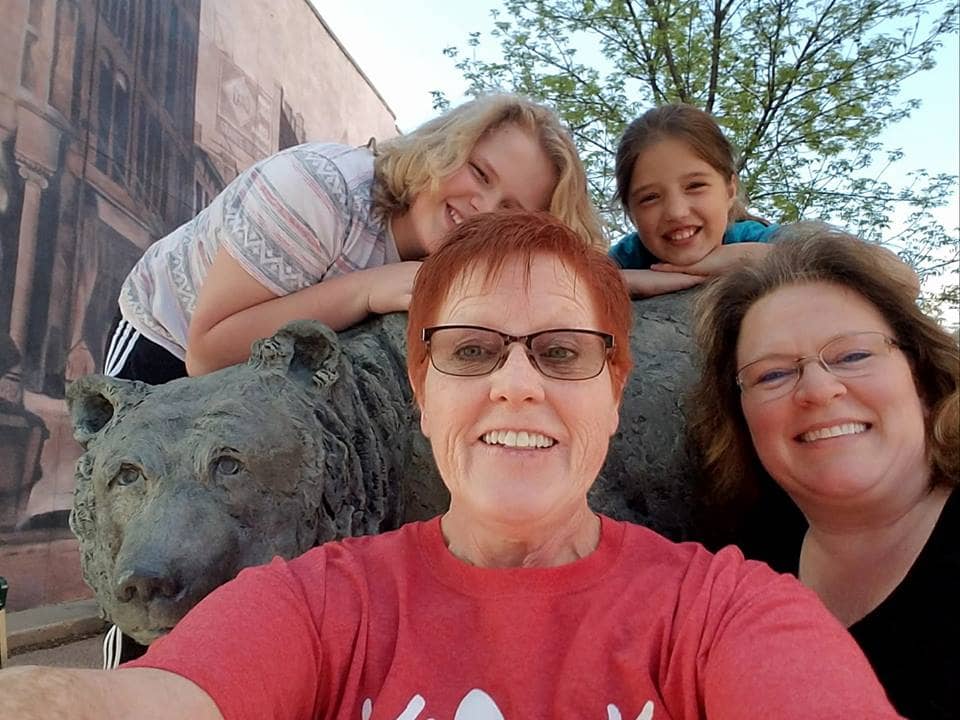 Two women standing in front of a bear statue with two children leaning on the top of the statue during a youth trip